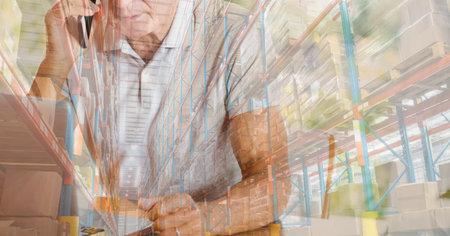 Caucasian man talking on the smartphone, using laptop computer at home shopping on line over warehouse with shelves full of cardboard parcel boxes in the background. Online shopping ecommerce social distancing and self isolation in quarantine lockdown concept digital composite.の写真素材