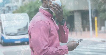 Digital illustration of a man wearing a face mask, walking on a street, using a smartphone over macro Coronavirus Covid-19 cells floating in the background. Medicine public health pandemic coronavirus Covid 19 outbreak concept digital composite.の写真素材