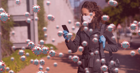 Digital illustration of macro Covid-19 cells floating over a woman wearing a face mask, using a...