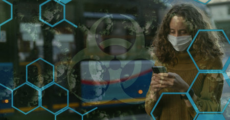 Digital illustration of a green hazard sign, macro Covid-19 cells floating over a woman wearing a face mask, using a smartphone. Coronavirus Covid-19 pandemic concept digitally generatedの写真素材
