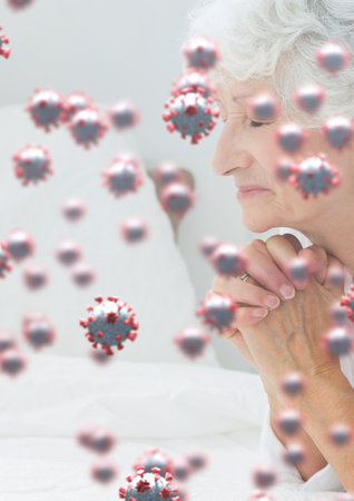 Digital illustration of macro Covid-19 cells floating over a Caucasian senior woman praying with her eyes closed. Religious faith in time of coronavirus global pandemic concept, digital composite.の写真素材
