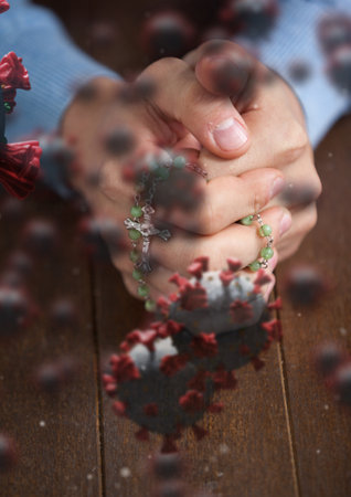 Digital illustration of macro Covid-19 cells floating over Caucasian hands holding a rosary,...