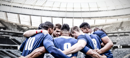 Team of multi-ethnic rugby players playing rugby at a sports stadium, wearing team strip, standing in a huddle, motivating before a game, digital composite.の写真素材