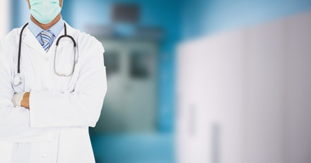 Mid section of male doctor wearing surgical gloves and protective face mask against coronavirus Covid-19, lab coat and stethoscope standing with arms crossed working in a hospital. Medicine public health pandemic coronavirus outbreak concept.の写真素材