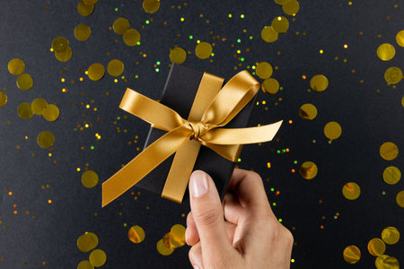 Composition of hand holding present and spots on gray background. Retail, shopping and black friday...