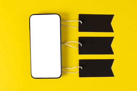 Composition of smartphone with gift tags on yellow background. Retail, shopping and black friday concept.の写真素材