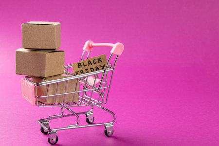 Composition of shopping cart with boxes and black friday text on pink background. Retail, shopping and black friday concept.の写真素材