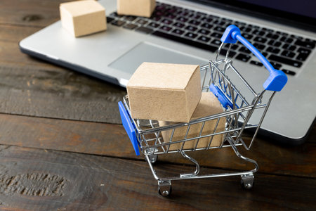 Composition of shopping cart with boxes and laptop on wooden background. Retail, shopping and black friday concept.の写真素材