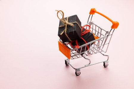 Composition of shopping cart with presents on pink background. Retail, shopping and black friday concept.の写真素材