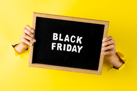 Composition of hands with black friday text on yellow background. Retail, shopping and black friday concept.の写真素材