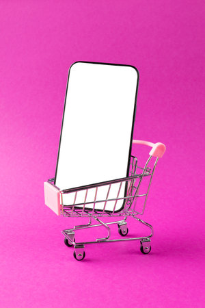 Composition of shopping cart and smartphone with copy space on pink background. Retail, shopping and black friday concept.の写真素材