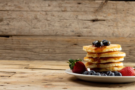 Horizontal image of stack of pancakes with blueberries and maple syrup, on wood with copy space....