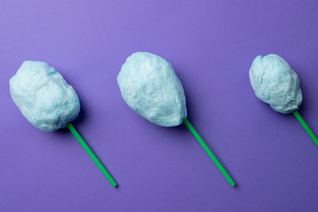 Horizontal image of homemade blue candy floss on three sticks, on purple background. Tasty home made sweet foods.の写真素材