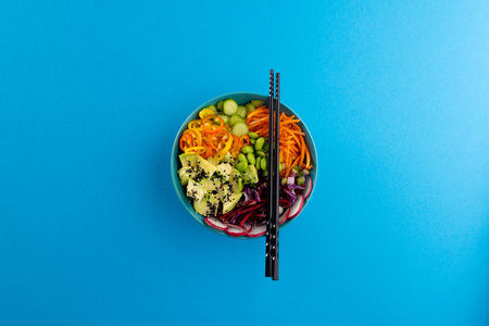 Overhead view of hawaiian poke bowl with chopsticks on blue background. Hawaiian tasty fresh food...