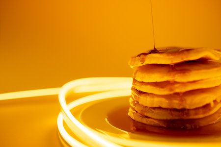 Horizontal image of maple syrup pouring onto stack of pancakes, yellow background and copy space. Food, organic ingredients and healthy eating.の写真素材