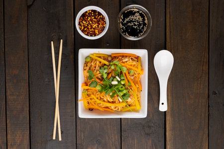 Overhead view of asian wok stir fry noodles and chopsticks, spoon and condiments on wood. Asian tasty home cooked food and healthy eating.の写真素材