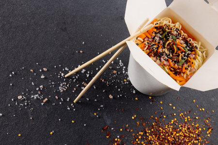 Overhead view of take away asian wok stir fry noodles with chopsticks in paper container on grey....