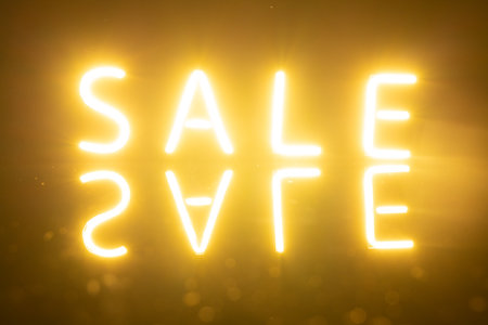 Image of glowing neon sale text with reflection over orange background. Retail, savings, shopping, light and colour concept.の写真素材