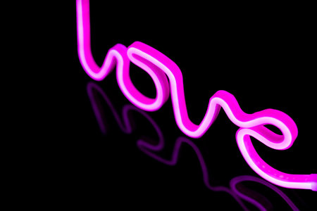 Image of vibrant neon love text formed with pink glow sticks over black background and copy space. Love, light and colour concept.の写真素材
