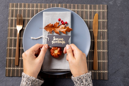 Overhead view of thanksgiving place setting with caucasian woman holding greetings tag on slate....