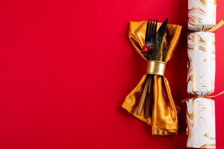 Image of place setting with cutlery, christmas cracker and copy space on red background. Christmas, tradition and celebration concept.の写真素材