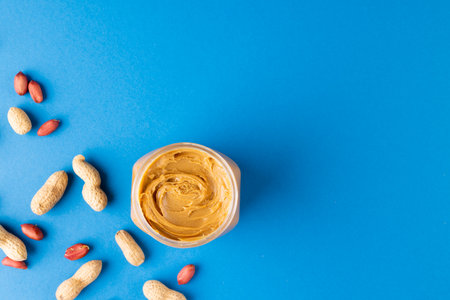 Image of peanut butter jar and nuts on blue background. Food, breakfast, nutrition and american...
