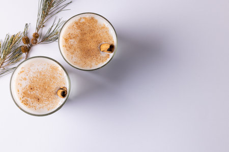 Image of two glasses of milk with cinnamon sticks christmas decorations copy space on white. Christmas, tradition and celebration concept.の写真素材