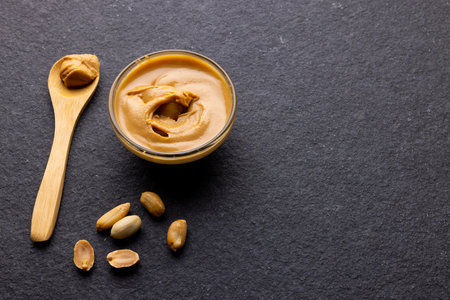Image of spoon and bowl with peanut butter and nuts on dark grey surface. Food, breakfast, nutrition and american cuisine concept.の写真素材