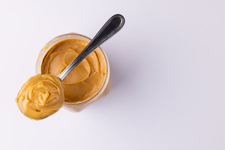 Image of spoon and jar with peanut butter on white surface. Food, breakfast, nutrition and american cuisine concept.の写真素材