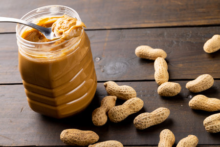 Image of jar with peanut butter and nuts on wooden surface. Food, breakfast, nutrition and american...