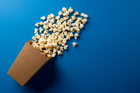 Image of pop corn scattered on blue surface. Food, snacks, cinema and american cuisine concept.の写真素材