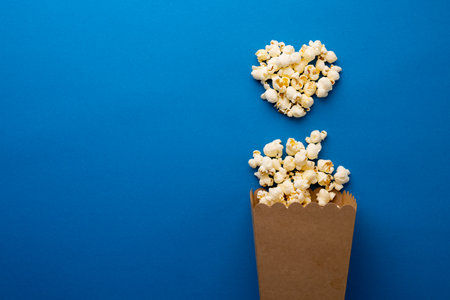 Image of heart made if pop corn on blue surface. Food, snacks, cinema and american cuisine concept.の写真素材