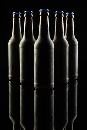 Vertical image of five dark glass bottles of lager beer with blue caps on black, with copy space. Drinking alcohol, refreshment and lager day celebration concept.の写真素材