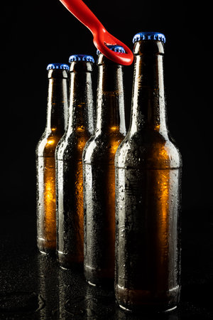 Image of red bottle opener and four beer bottles with blue crown caps, with copy space on black. Drinking alcohol, refreshment and lager day celebration concept.の写真素材