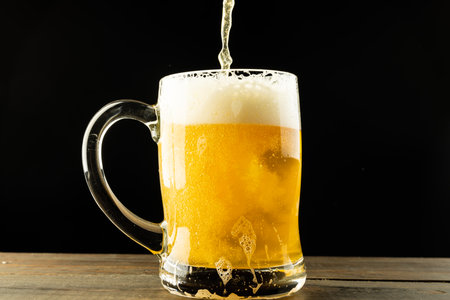 Image of beer pouring into glass tankard of foamy beer on wooden table, with copy space. Drinking alcohol, refreshment and lager day celebration concept.の写真素材