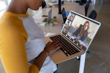 Midsection of african american woman talking on video conference with coworkers at office. Unaltered, meeting, business, finance, communication and technology concept.の写真素材