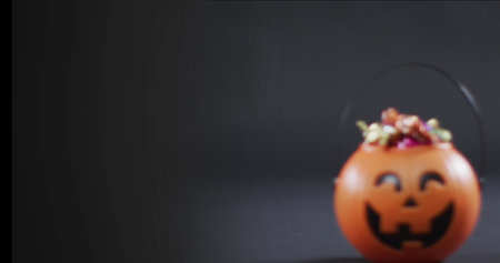 Image of halloween text over carved pumpkin bucket with sweets on black background. Halloween, autumn, fall, festivity tradition and celebration concept digitally generated image.の写真素材