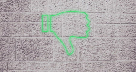Composite of illuminated digital green dislike button icon against gray wall, copy space. Thumbs down, social media, negative emotion, hand, symbol and feedback concept.の写真素材