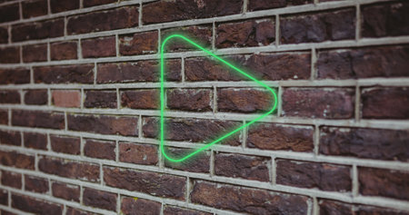 Composite of illuminated digital green play button icon against brick wall, copy space. Music, movie, multimedia, playing, pushing, symbol, control and technology concept.の写真素材