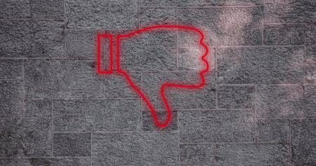 Composite of illuminated digital red dislike button icon against gray wall, copy space. Thumbs down, social media, negative emotion, hand, symbol and feedback concept.の写真素材