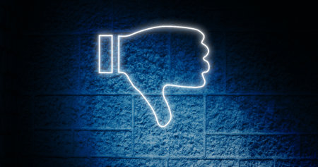 Composite of glowing dislike button icon against blue wall, copy space. Thumbs down, social media, illuminated, dark, negative emotion, hand, symbol and feedback concept.の写真素材