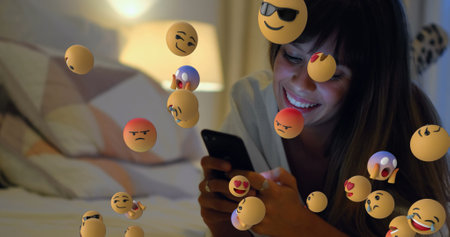 Image of emoticons over happy caucasian woman lying with smartphone in bed. Social media,...