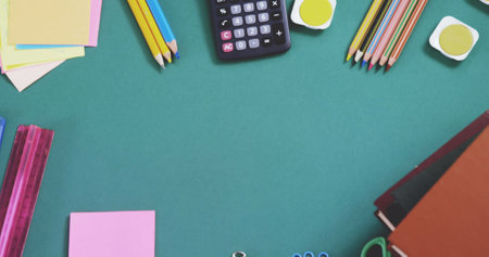 Overhead view of multicolored pencils with calculator, ruler, sticky notes and books on blue table....