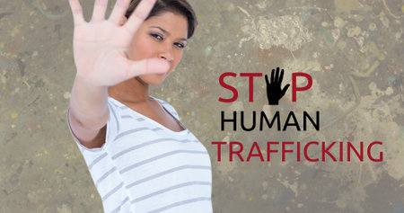 Composite of stop human trafficking text over biracial woman showing stop sign against gray wall. Gesture, copy space, crime, freedom, awareness and prevention concept.の写真素材