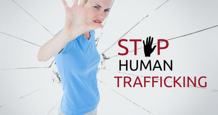 Composite of stop human trafficking text over caucasian woman showing stop sign against broken glass. Copy space, alertness, crime, freedom, awareness and prevention concept.の写真素材