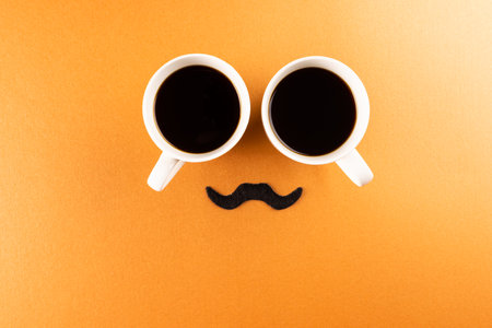 Composition of fake moustache and cups of coffee on orange background with copy space. Fake moustache day, party, celebration and costume concept.の写真素材