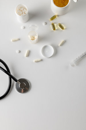 Vertical composition of stethoscope with syringe and pills on white background with copy space. Medical services, healthcare and health awareness concept.の写真素材