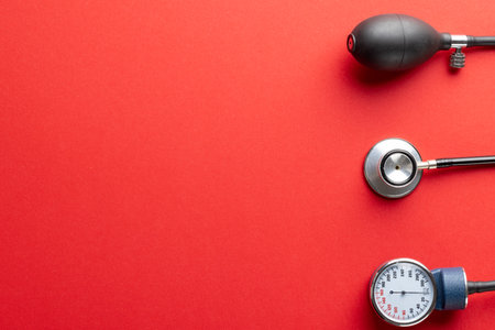 Composition of sphygmomanometer and stethoscope on red background with copy space. Medical services,...