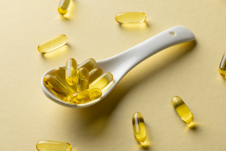 Composition of oil capsules and white spoon on yellow background. Medicine, medical services, healthcare and health awareness concept.の写真素材