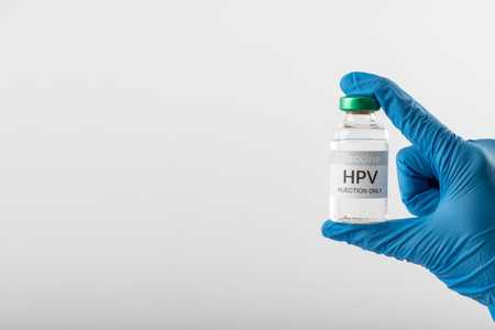 Composition of gloved hand holding hpv vaccine vial on white background with copy space. Medicine, medical services, healthcare and health awareness concept.の写真素材